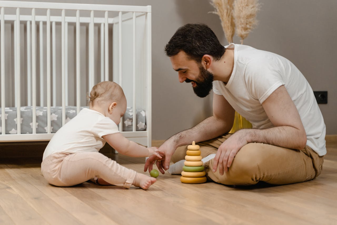Father and baby playing with wooden toys on floor, showcasing joyful parenting moments.